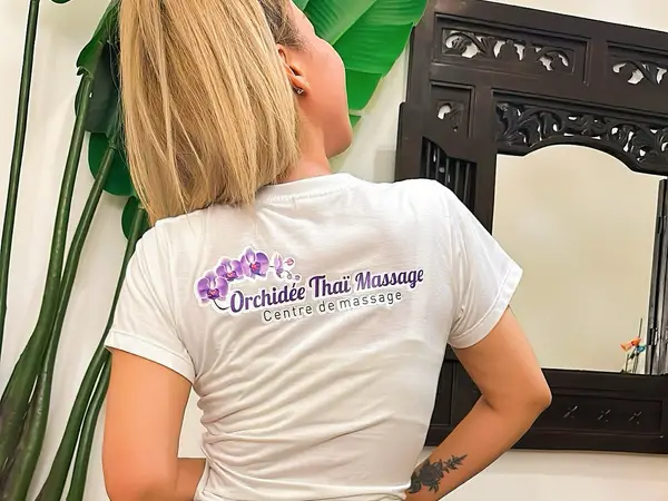 Woman in white salon shirt stands beside leafy decor and carved mirror