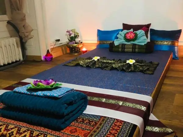Thai massage room with low bed, folded towels, and soft warm lighting