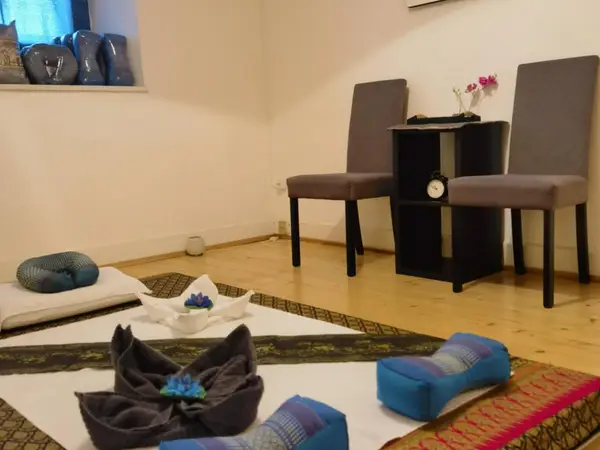Cozy Thai massage room with mats, cushions, chairs, and a small side table