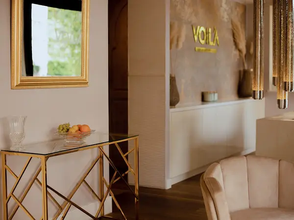 Elegant spa reception with gold accents, mirror, fruit bowl, and beige chair