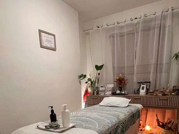 Cozy massage room with treatment bed, candles, plants, and curtained window
