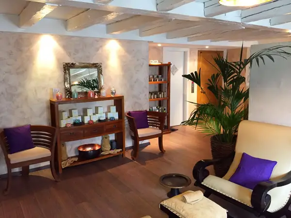 Warm spa waiting room with wooden chairs, purple cushions, and potted palm