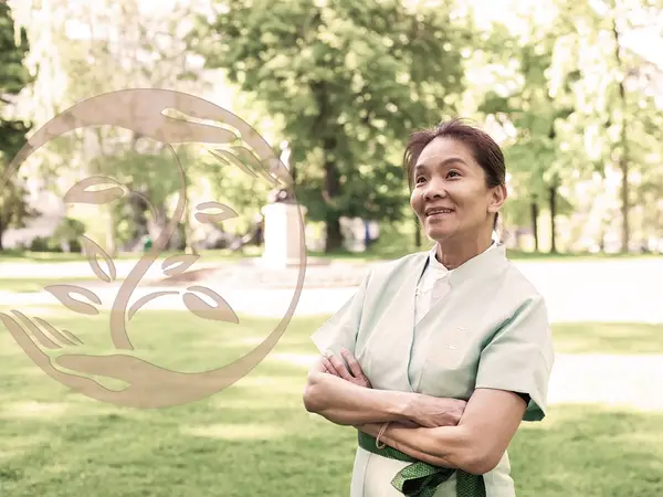 Woman in a light uniform standing outdoors in a sunny park-like setting