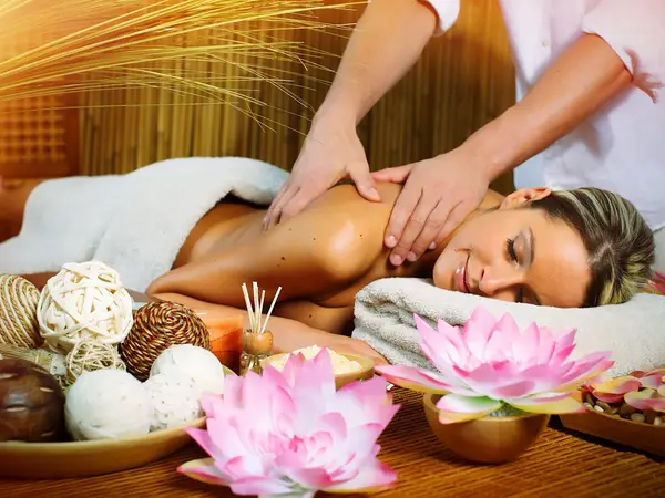 Spa massage room with a client receiving back massage beside decorative flowers and candles