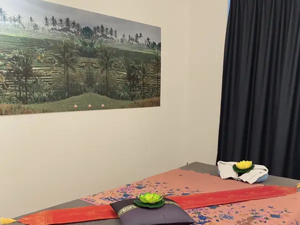 Massage room with Thai decor, wall art, curtains, and a treatment table
