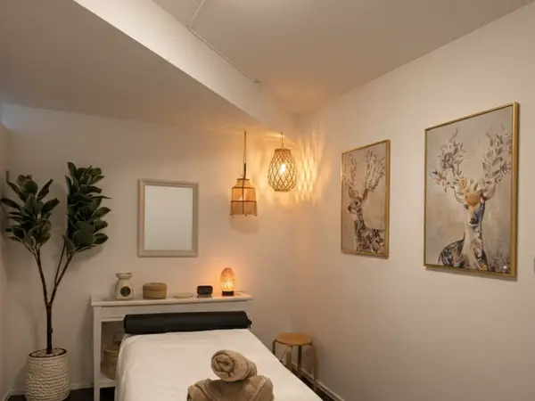 Cozy massage room with treatment bed, warm lighting, deer artwork, and potted plant
