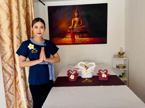 Massage room with therapist, decorated treatment bed, Buddha artwork, and floral towels