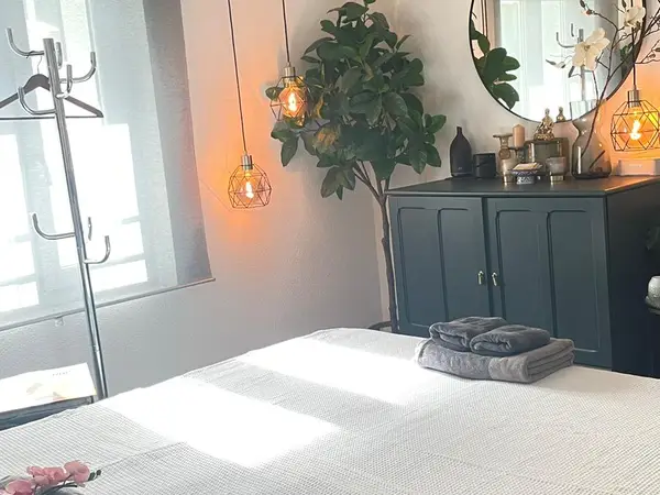 Cozy massage room with bed, hanging lights, cabinet, mirror, and plant