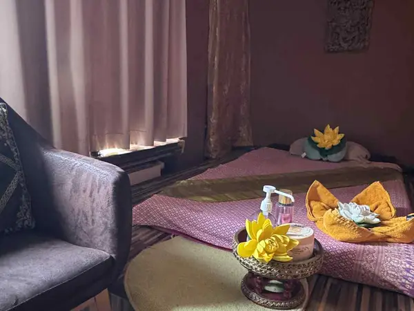 Dim massage room with low mat, chair, curtains, and floral decor