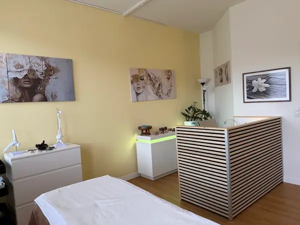 Bright massage room with treatment bed, striped counter, and floral wall art