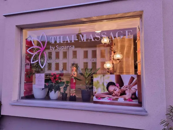 Thai massage storefront window with plants, warm lights, and a massage poster