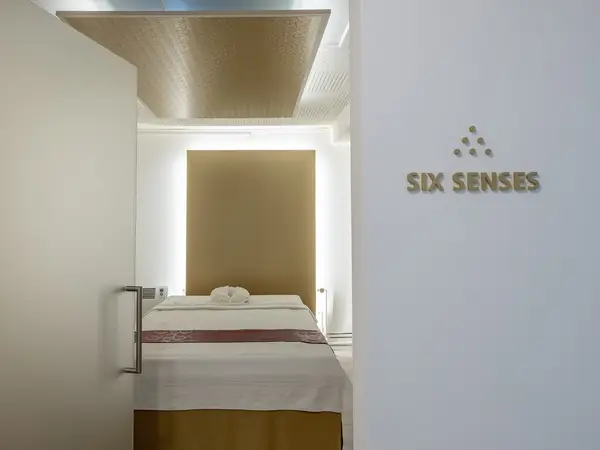 Minimalist massage room with treatment bed and Six Senses sign on white wall