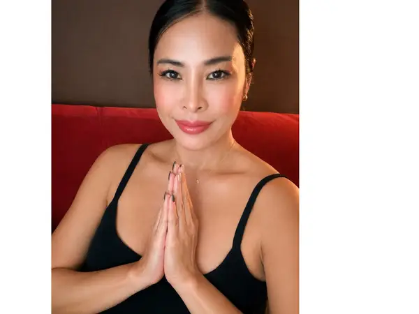 Woman posing indoors with hands together on a red couch against a dark wall