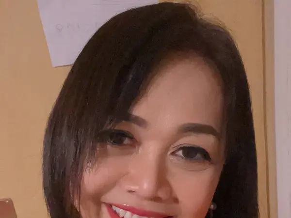 Close-up of a smiling woman against a plain indoor wall