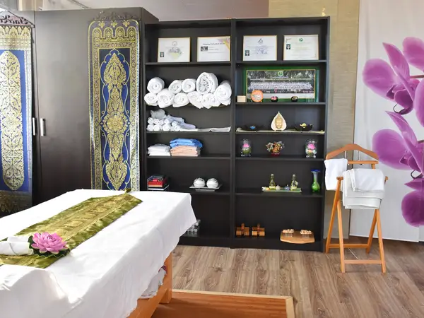 Thai-massage treatment room with bed, black shelving, towels, and purple floral decor