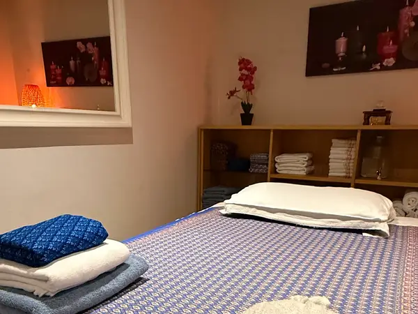 Cozy massage room with mat, folded towels, shelves, and warm lighting