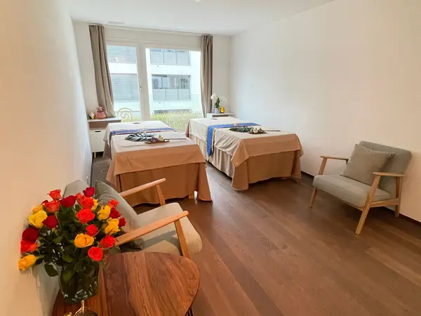 Bright massage room with two treatment tables, chairs, and flowers by a window