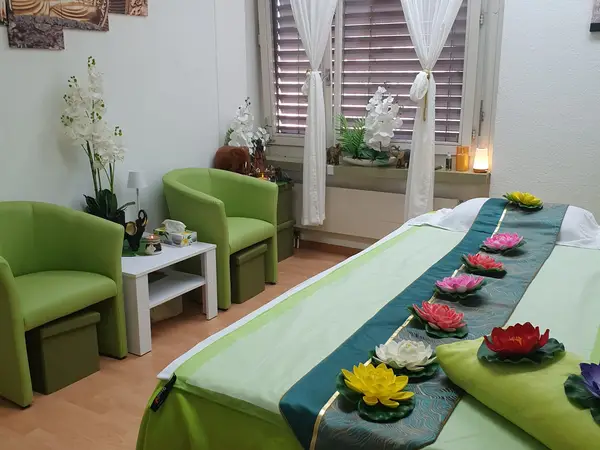 Bright massage room with green chairs, floral decor, and a treatment bed with lotus flowers