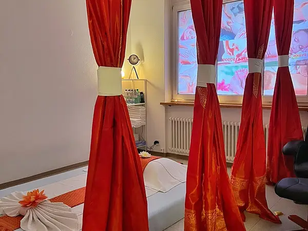 Massage room with red curtains, a treatment mat, and warm ambient lighting