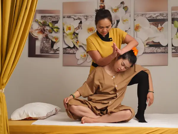 Thai massage treatment room with floral wall art and yellow curtains, two women inside