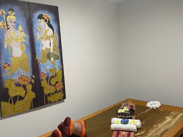 Thai massage room with a low mat, rolled towels, and Thai wall art