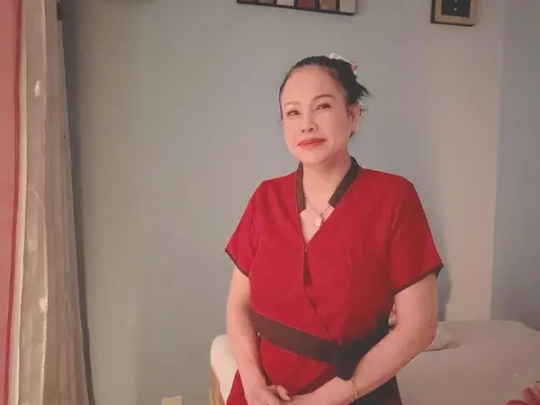 Massage room with a red-uniformed woman beside a treatment table