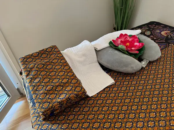 Massage table with patterned cover, towels, pillows, and pink lotus decor indoors