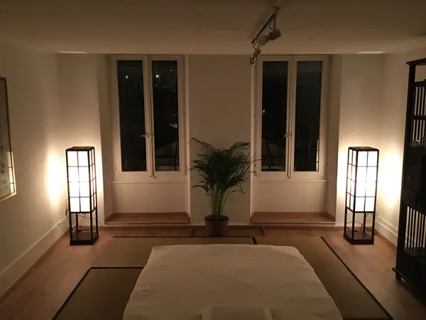 Dim massage room with table, glowing floor lamps, and a potted plant
