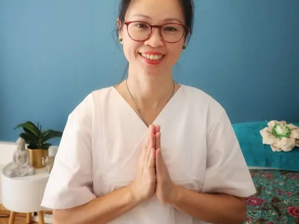 Smiling therapist in white uniform with hands pressed together in treatment room