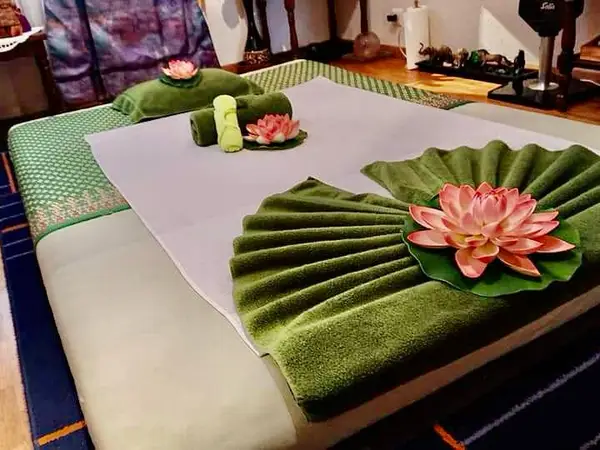 Thai massage room with neatly made bed, green towels, and lotus decorations