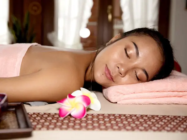 Woman resting on a massage table with pink towels in a serene spa room