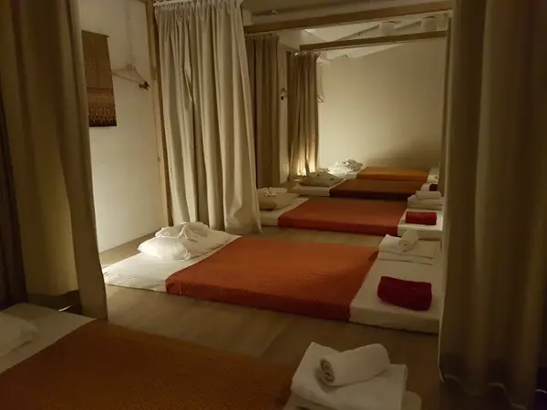 Dim massage room with several floor mats and folded towels separated by curtains