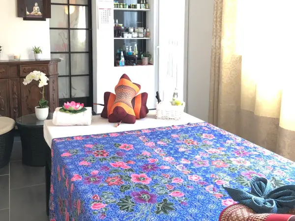 Bright massage room with floral bedspread, cushions, and Thai-style decor