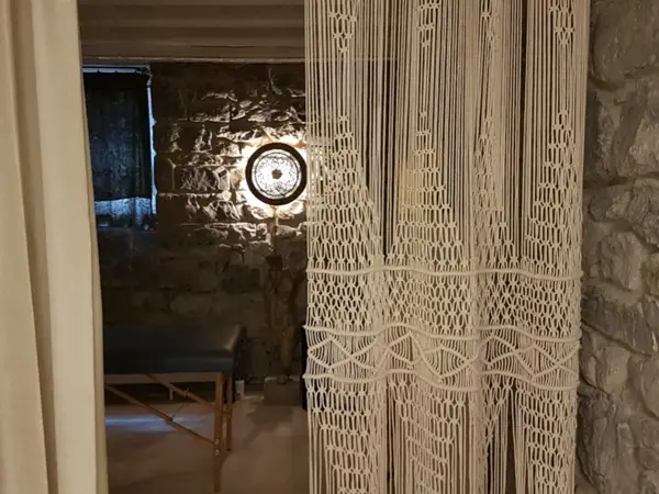 Dim massage room with stone walls, a treatment table, and a macramé curtain