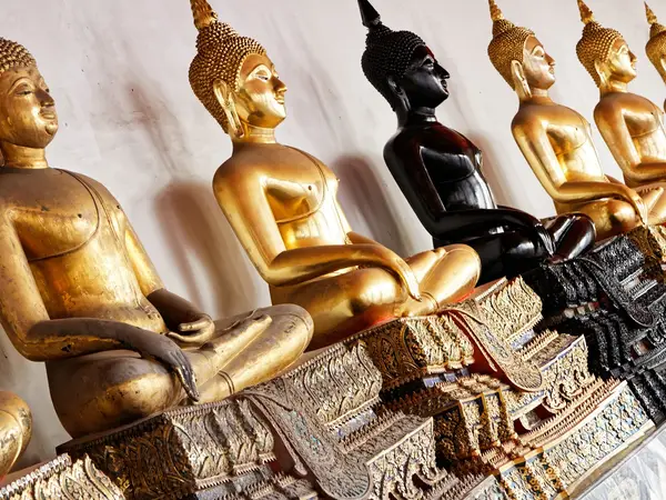 Row of golden and black Buddha statues on ornate carved pedestals