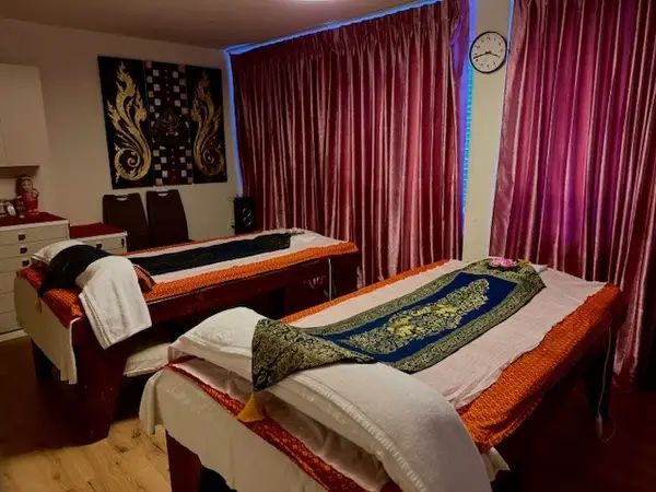 Thai massage room with two massage beds, pink curtains, and warm lighting