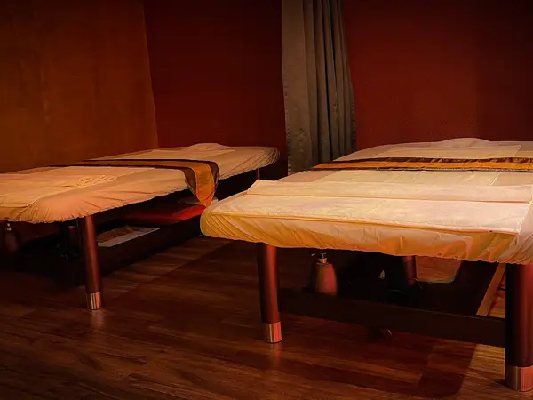 Dim massage room with two treatment tables and dark wood flooring