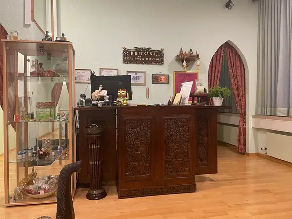 Thai spa reception with carved wooden desk, display cabinet, and curtained window