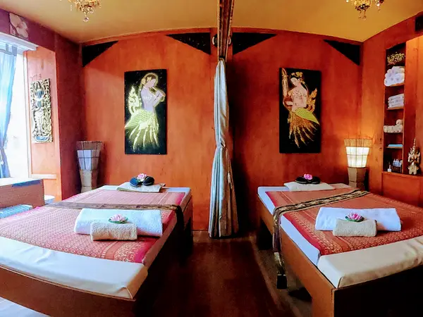 Warm Thai massage room with twin treatment beds, orange walls, and soft lamps