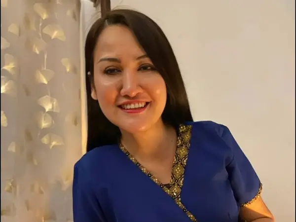 Smiling woman in blue Thai-style uniform beside patterned curtain indoors