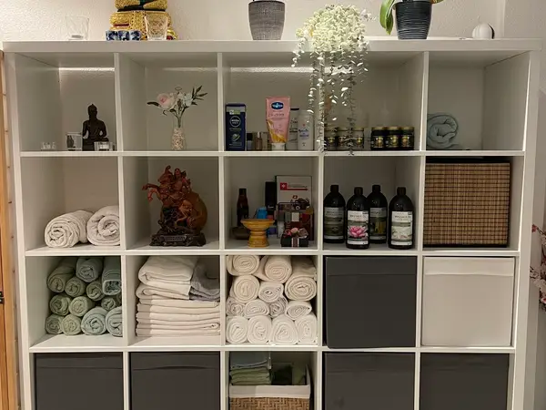 White cubby shelf with rolled towels, massage products, and small decor