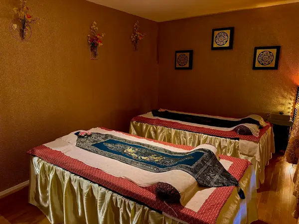 Warm massage room with two neatly made treatment beds and wall art