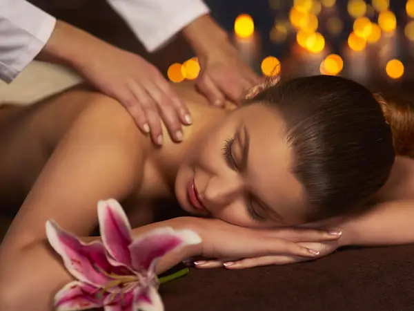 Massage therapist kneads a resting woman in a softly lit spa room