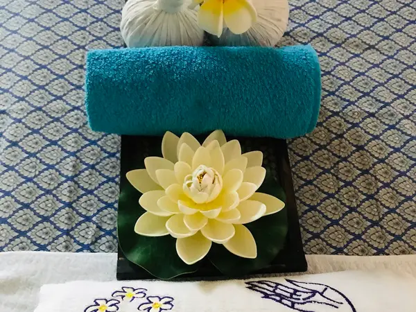Decorative massage room setup with folded towel, lotus flowers, and patterned fabric backdrop