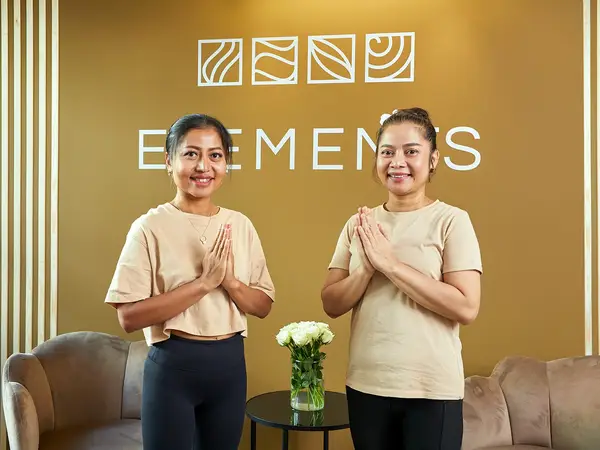 Two smiling staff members stand in a warm spa lobby with ELEMENTS signage
