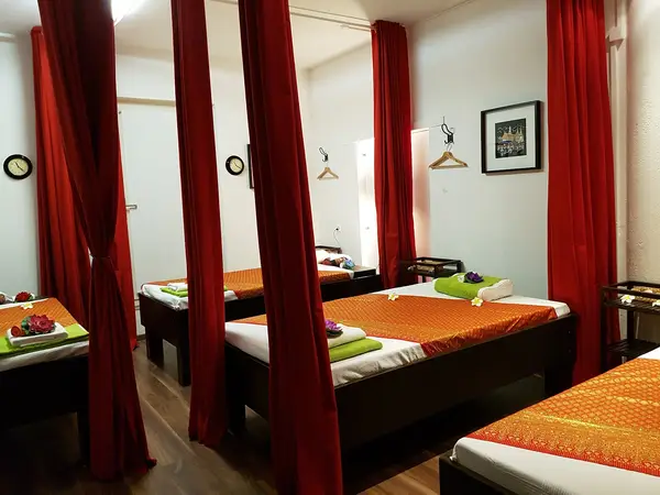 Massage room with red curtains, neatly made treatment beds, and framed wall art