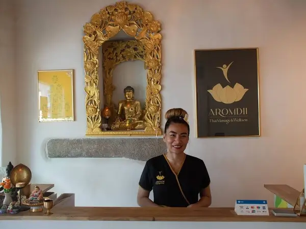 Thai massage reception with gold Buddha decor and smiling staff member