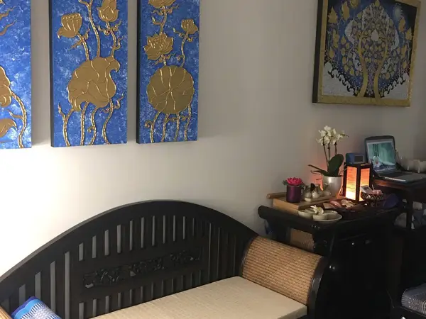 Cozy massage room with Thai artwork, dark wood bench, and soft ambient lighting