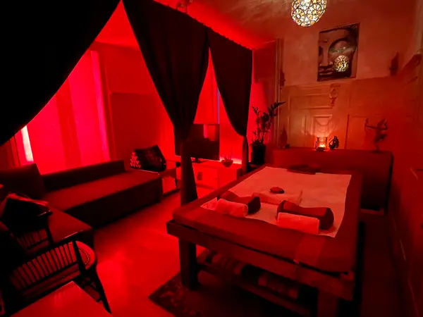 Red-lit massage room with treatment table, curtains, and candles