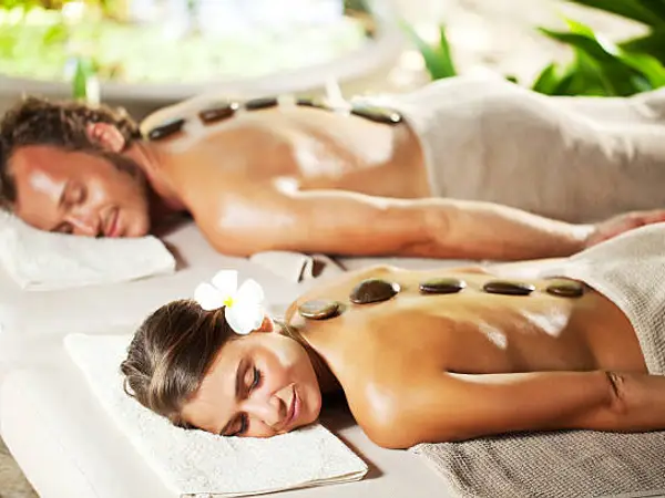 Two spa clients receive hot stone massages on treatment tables